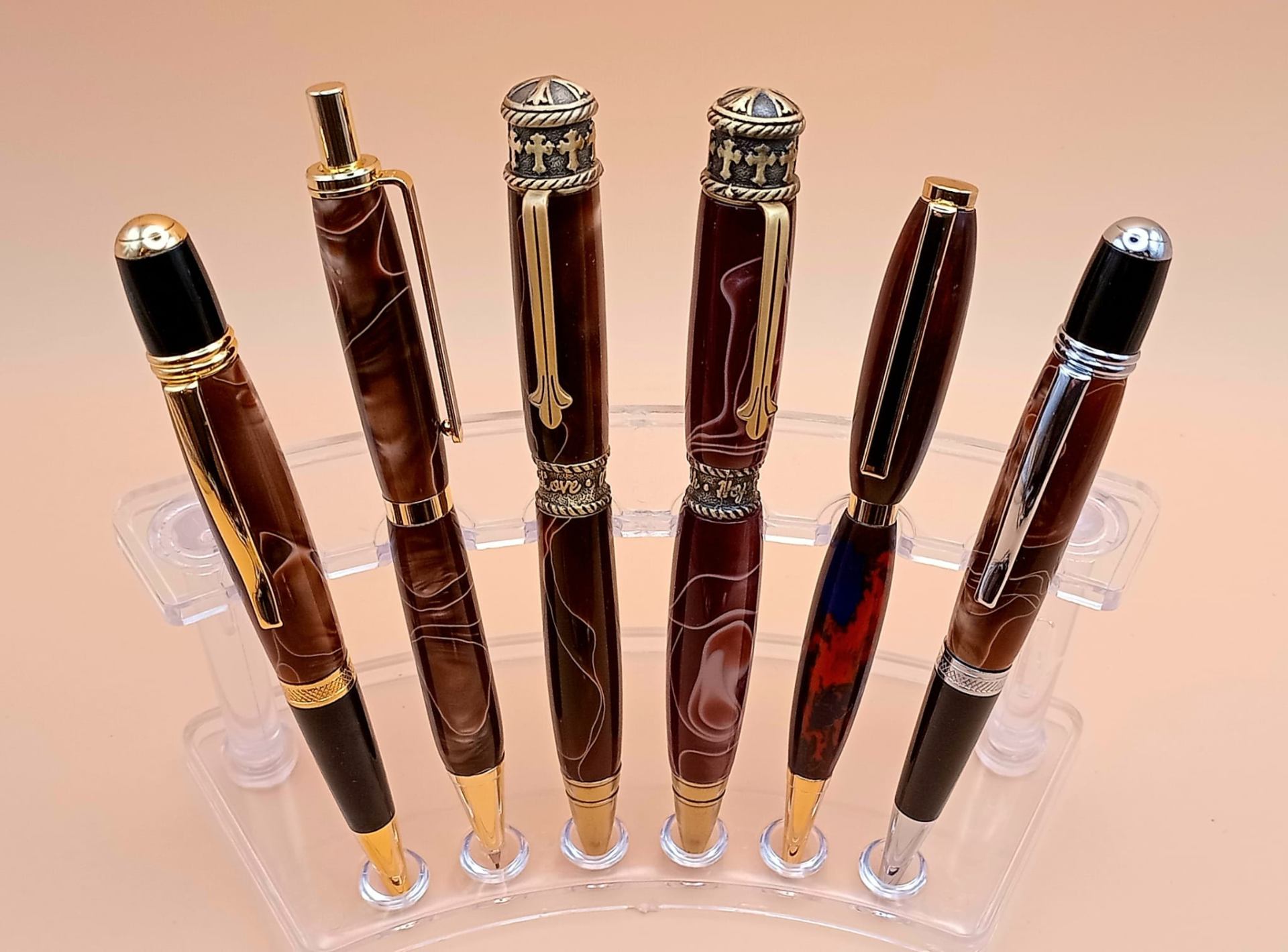 Religious cross-top resin pens alongside marbled brown swirl artisan pens with gold fittings